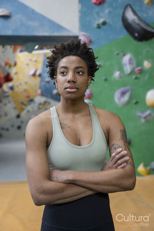 Portrait of serious woman standing with arms crossed in front of climbing wall