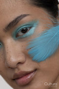 Portrait of woman with blue makeup and feather on face