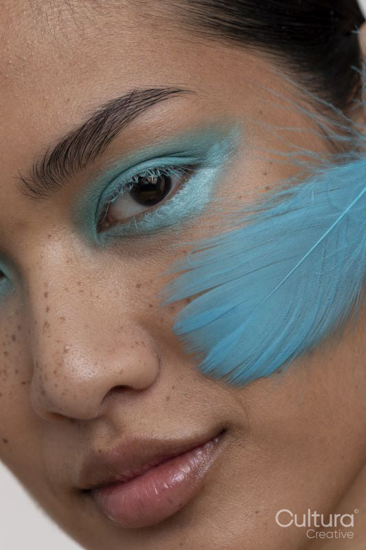 Portrait of woman with blue makeup and feather on face