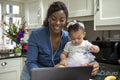 Woman working on laptop at home and taking care of baby daughter