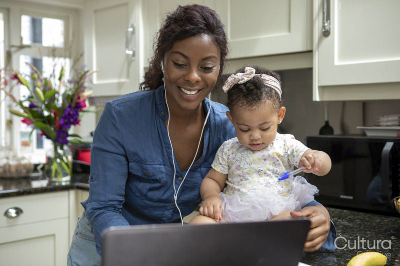 Woman working on laptop at home and taking care of baby daughter