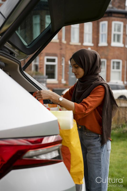 Woman wearing hijab unloading shopping bags from car trunk
