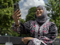 Sutton,Woman in headscarf sitting on bench in park,talking on smart phone