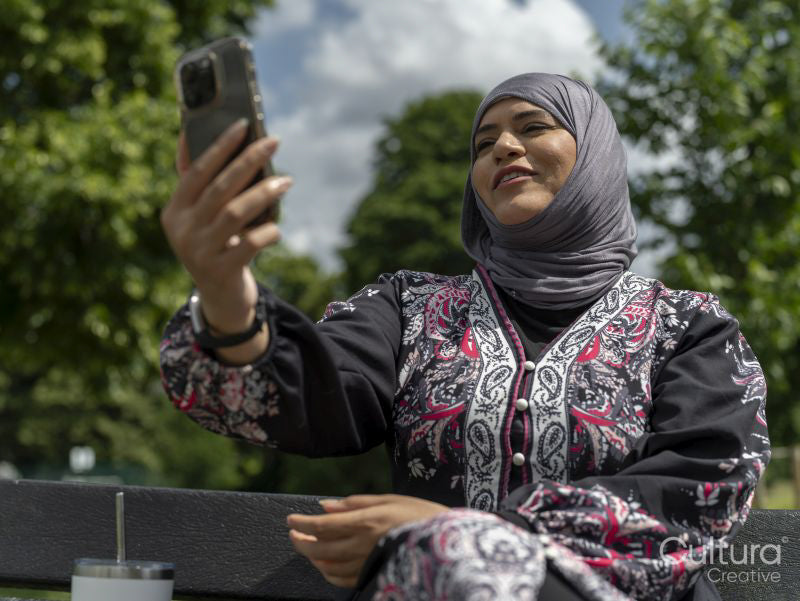 Sutton,Woman in headscarf sitting on bench in park,talking on smart phone