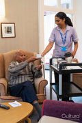 Female employee serving tea to senior man in nursing home