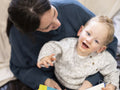 Smiling boy with cerebral palsy sitting on mothers lap