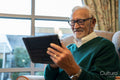 Senior man sitting in armchair and using tablet in nursing home