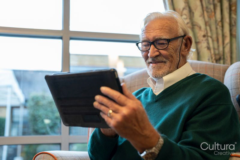 Senior man sitting in armchair and using tablet in nursing home