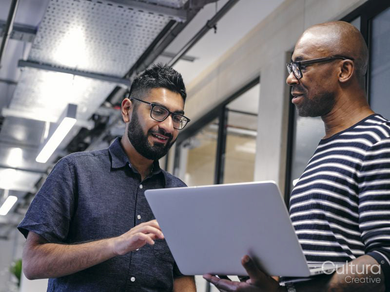 Two men in office hallway, looking at laptop