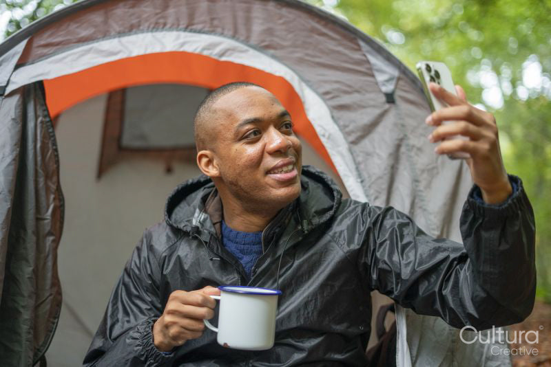 Man taking selfie outside of tent and holding metal mug