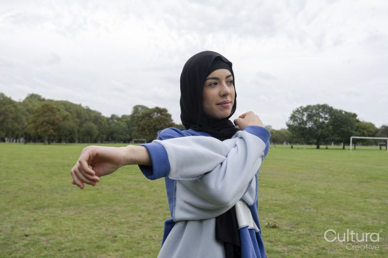 Portrait of woman in hijab stretching arm in park