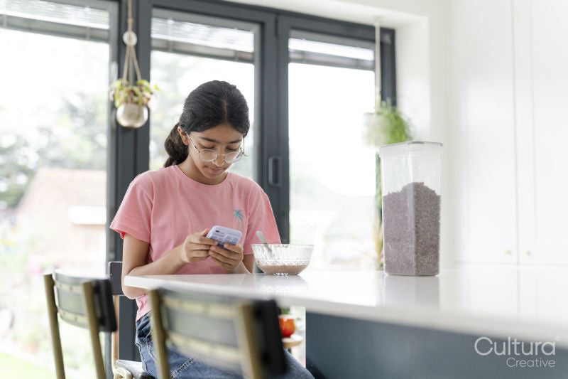 Girl eating breakfast and using phone at table in living room