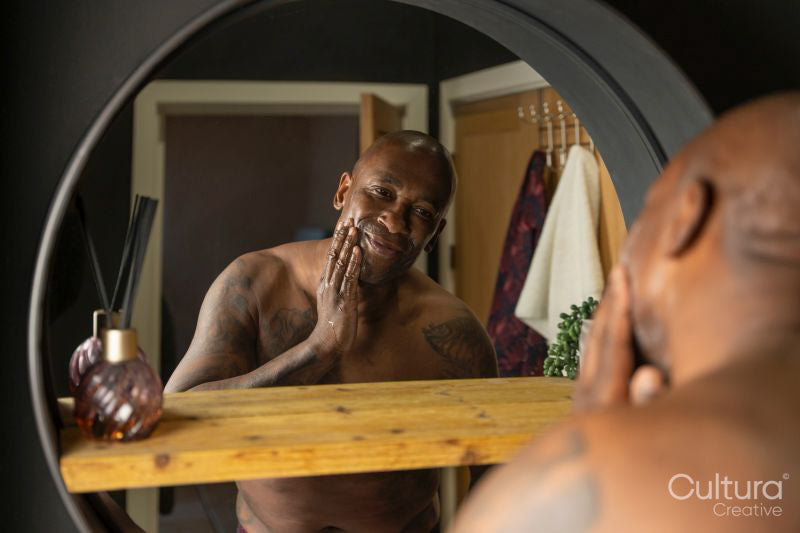 Man reflecting in bathroom mirror while applying face cream