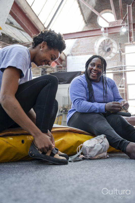Mother and daughter putting on climbing shoes while sitting on mattress