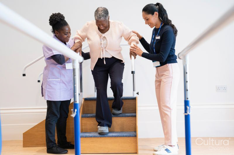 Female therapist and nurse assisting senior woman descending steps in exercise room