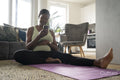 Smiling pregnant woman sitting on yoga mat with smart phone