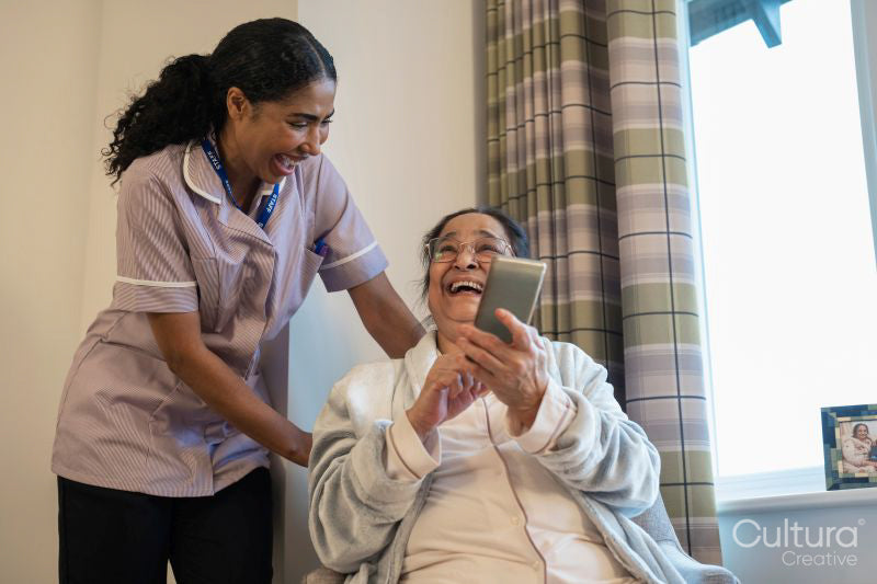 Senior lady looking at phone with nurse in room at nursing home