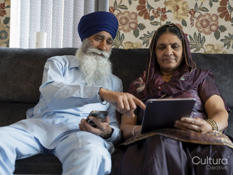 Senior couple in traditional clothing using phone and tablet at home