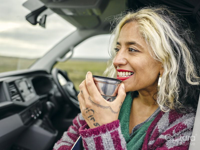 Woman sitting in van and drinking from insulated drink container
