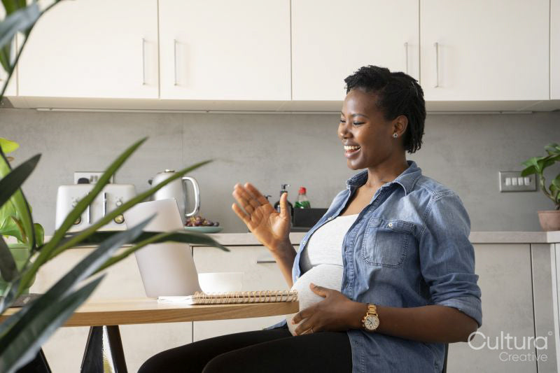 Smiling pregnant woman having video call via laptop in kitchen