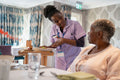 Nurse serving meal to senior woman in nursing home