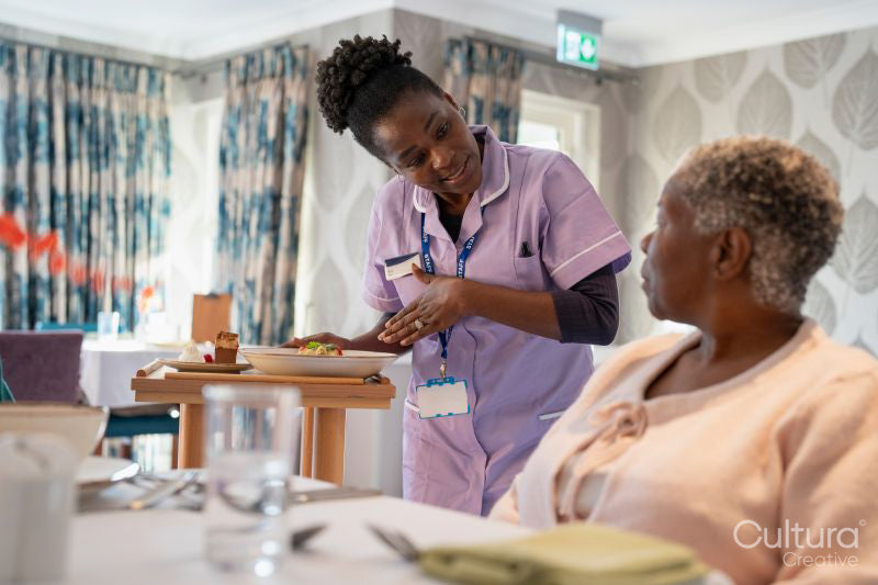Nurse serving meal to senior woman in nursing home
