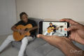 Teenage boy recording friend playing guitar at home