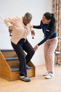 Female therapist assisting senior woman descending steps in exercise room