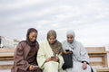 Three Muslin women using smart phones while sitting on bench