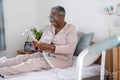 Smiling senior woman in bathrobe sitting on bed, holding remote control
