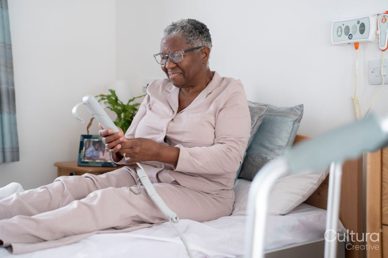 Smiling senior woman in bathrobe sitting on bed, holding remote control