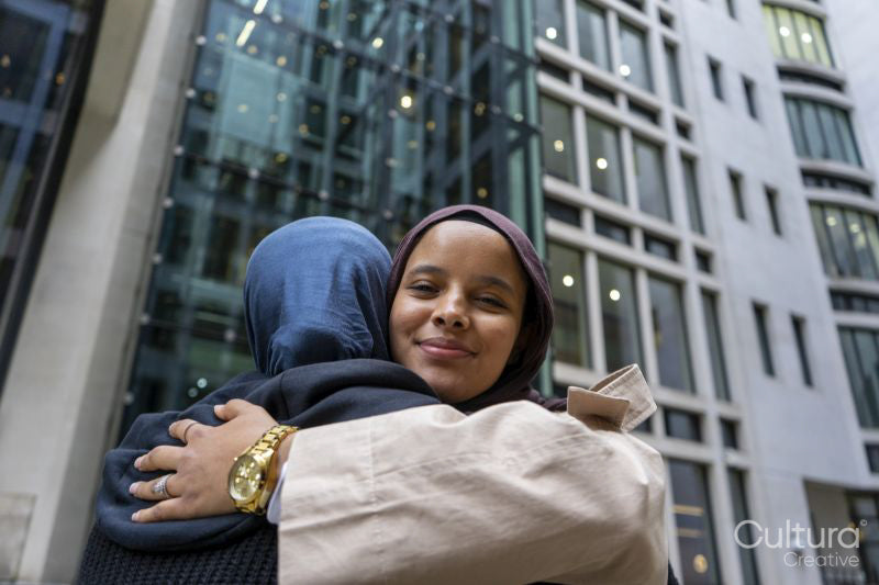 Two women wearing hijabs hugging in street