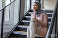 Portrait of smiling woman wearing headscarf sitting on steps and holding cup