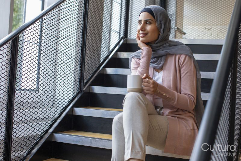 Portrait of smiling woman wearing headscarf sitting on steps and holding cup