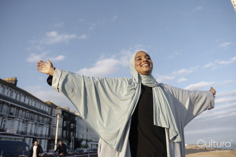 Portrait of smiling Muslim woman standing with arms outstretched on sunny day