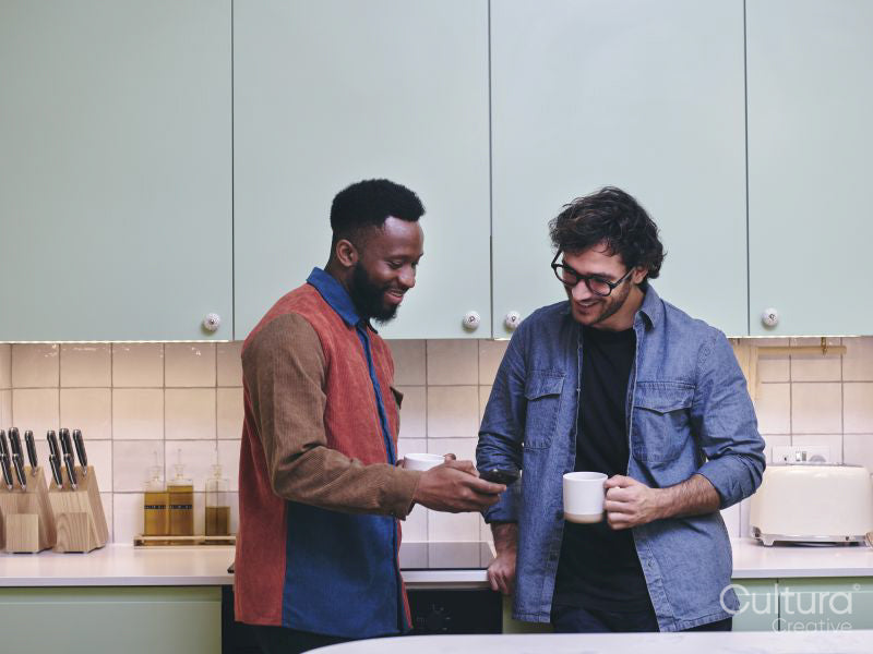 Two smiling men looking at smart phone in kitchen