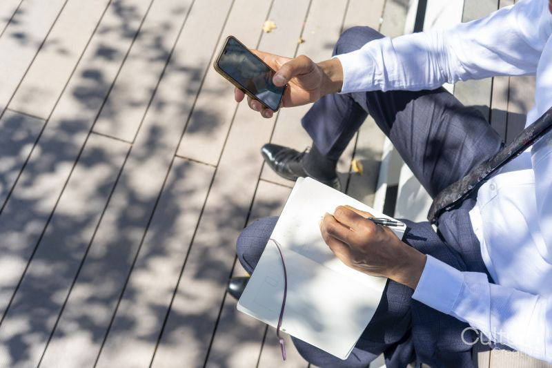 Businessman using phone and taking notes outdoors