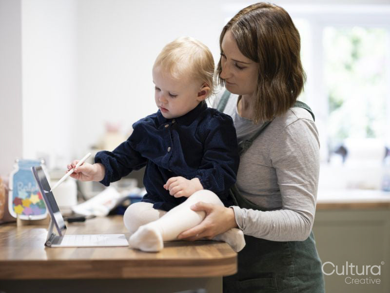 Mother standing by daughter drawing on digital tablet