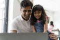 Father sitting with daughter and using laptop