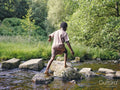 Boy walking on rocks in shallow creek