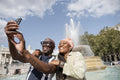 Happy mature couple taking selfie next to fountain in Trafalgar Square