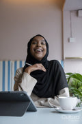 Smiling young woman in hijab working on tablet in cafe
