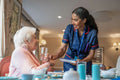 Nurse giving pill to senior lady during dinner at cafeteria in nursing home