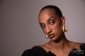 Woman in a black dress with gold earrings on a grey background