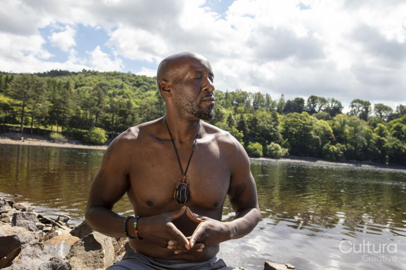 Shirtless man meditating on lakeshore, Yorkshire, UK
