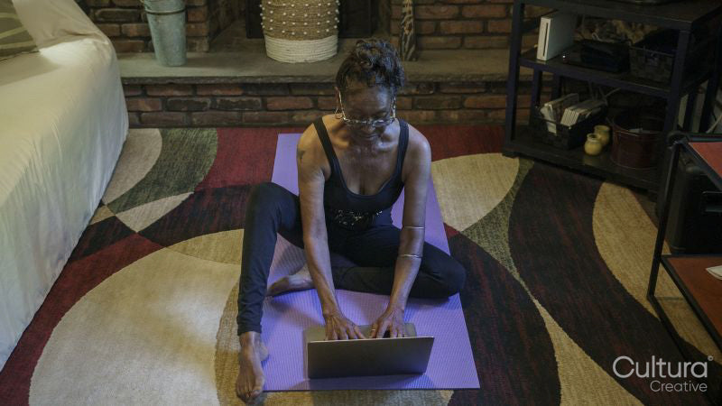 Senior woman sitting on yoga mat and using laptop