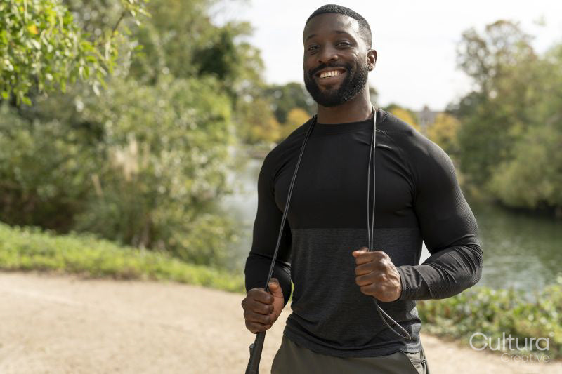 Portrait of smiling athletic man with jump rope in park