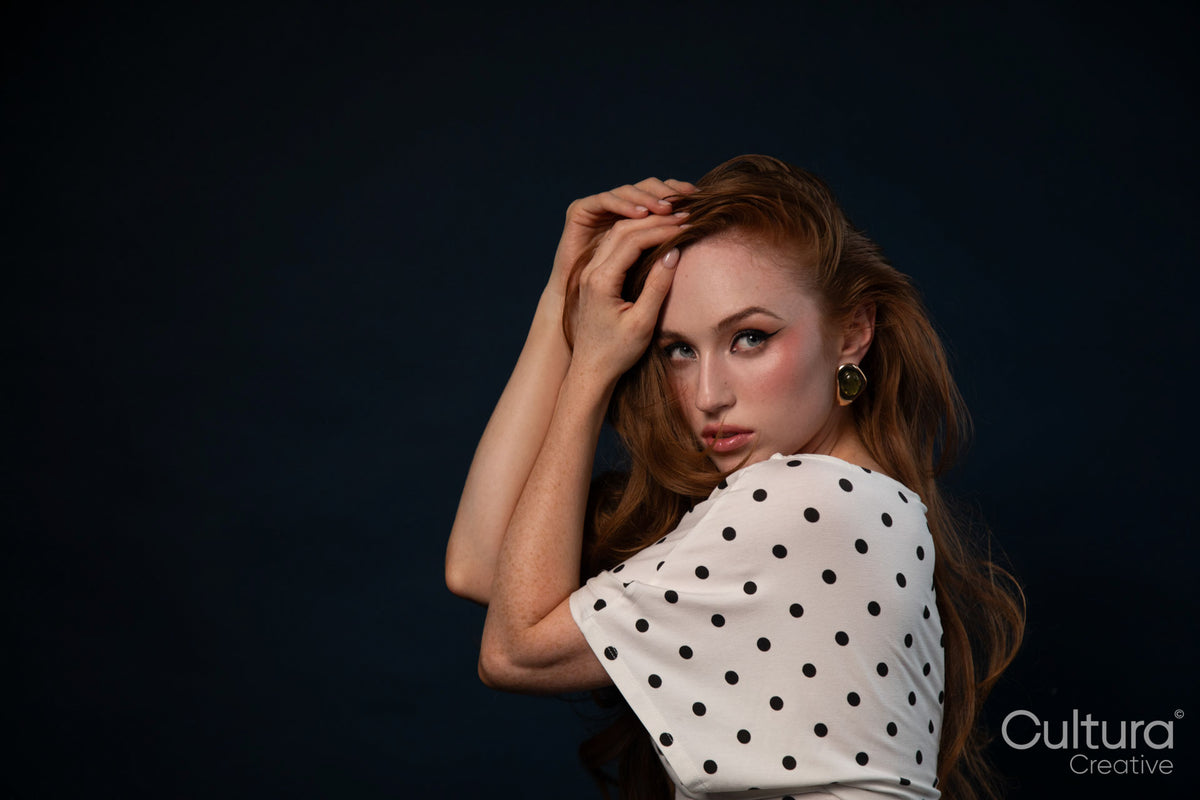 Woman posing with hand on head in polka dot top studio portrait