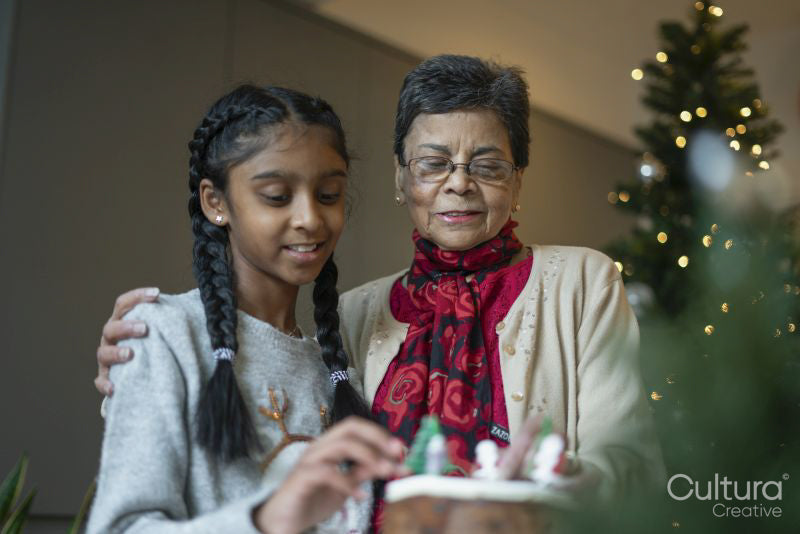 Smiling girl with grandmother decorating Christmas cake