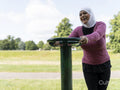 Sutton,Smiling woman in headscarf exercising at park gym
